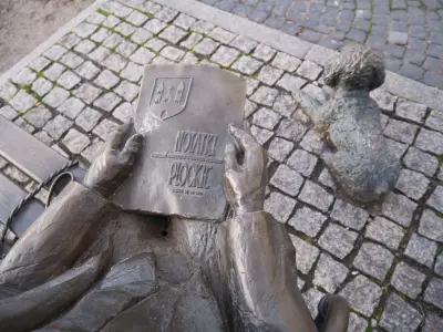 Brązowa postać na ławeczce trzymająca księgę „Notatki Płockie” oraz rzeźba psa na brukowanym chodniku