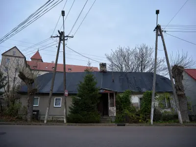 Zniszczony parterowy dom przy ulicy Klasztornej w Czerwińsku nad Wisłą, na tle murów i wież klasztoru