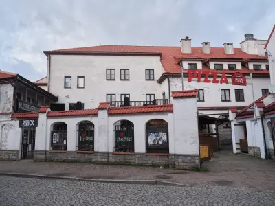 Biała kamienica z czerwonym dachem i szyldem PIZZA przy brukowanej ulicy w Płocku