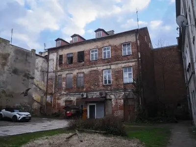Zniszczona ceglana kamienica oficynowa na podwórzu przy ulicy Długiej w Płocku, z muralem ptaka na sąsiedniej ścianie i 