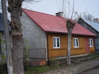 Drewniany parterowy dom z czerwonym dachem przy ulicy, z przyciętymi drzewami i chodnikiem w Czerwińsku nad Wisłą