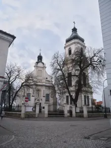 Barokowy kościół św. Bartłomieja i wysoka wieża dzwonnicy w Płocku, widziane zimą zza brukowanej ulicy i żelaznego ogrod