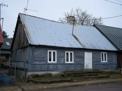 Parterowy drewniany dom z blaszanym dachem, białymi oknami i drzwiami przy ulicy w Czerwińsku nad Wisłą