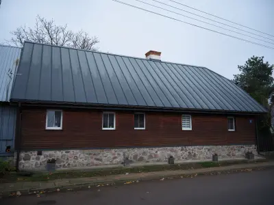 Długi drewniany dom z kamienną podmurówką i ciemnym metalowym dachem przy spokojnej ulicy