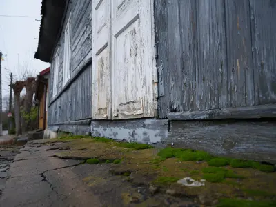 Zbliżenie na obdrapane białe drzwi starego drewnianego domu i omszały próg w Czerwińsku nad Wisłą