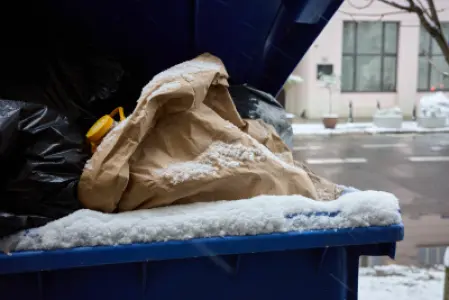 Niebieski kontener na śmieci ze śniegiem i workami odpadów przy ulicy w Warszawie