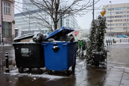 Przepełnione kontenery na śmieci przy ośnieżonym chodniku ulicy Bagatela w centrum Warszawy