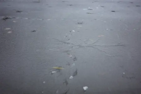 Zbliżenie zamarzniętej tafli stawu w Łazienkach Królewskich z widocznymi pęknięciami lodu