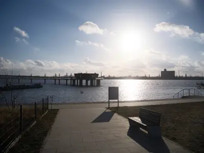 Promenada z ławką nad Wisłą w Płocku, widok na betonowe molo portowe i zabudowania przemysłowe po drugiej stronie rzeki