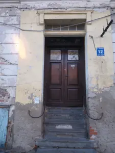 Zniszczone wejście do kamienicy przy ulicy Kościuszki 12 w Płocku, z betonowymi schodami i starymi drewnianymi drzwiami