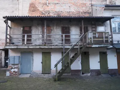 Stara oficyna kamienicy w Płocku z drewnianą galerią, schodami i rzędem zielonych drzwi na podwórku