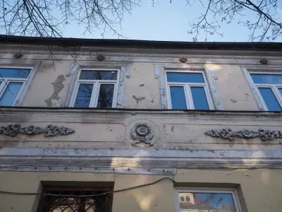 Górna część fasady starej kamienicy w Płocku z trzema oknami i bogatą sztukaterią kwiatową