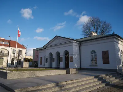 Biały klasycystyczny Dom Broniewskiego przy ul. Tumskiej w Płocku z granitowymi schodami i masztem z polską flagą zimą