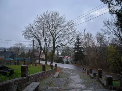 Brukowane zejście ulicy Klasztornej w Czerwińsku nad Wisłą z kamiennymi murkami i domami na tle drzew