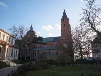 Bazylika katedralna w Płocku zimą, widoczna wieża i kopuła od strony ulicy Mostowej, z przyległym budynkiem i skwerem na